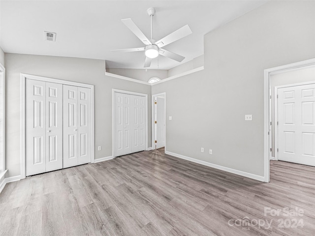 unfurnished bedroom with vaulted ceiling, ceiling fan, hardwood / wood-style flooring, and multiple closets