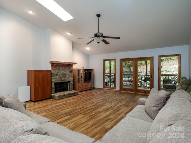 living room featuring a stone fireplace, hardwood / wood-style floors, ceiling fan, and lofted ceiling with skylight