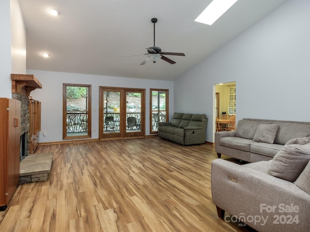 living room with a skylight, a fireplace, light hardwood / wood-style floors, ceiling fan, and high vaulted ceiling