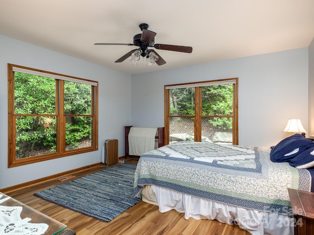 bedroom with radiator heating unit, multiple windows, hardwood / wood-style flooring, and ceiling fan