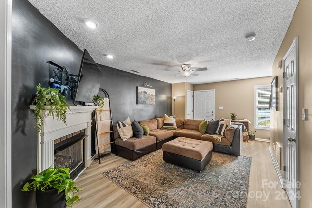 living room featuring light wood-type flooring, ceiling fan, and a textured ceiling