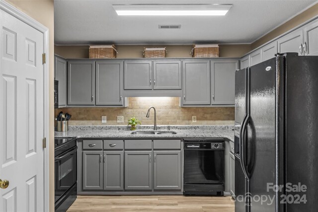 kitchen featuring gray cabinetry, light hardwood / wood-style flooring, light stone counters, sink, and black appliances