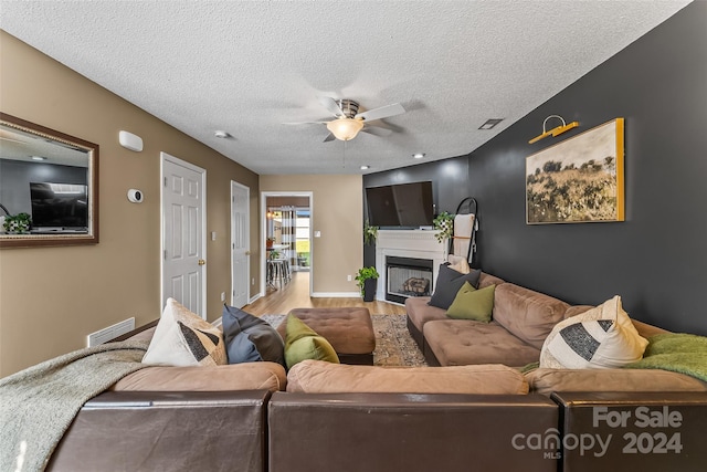 living room with ceiling fan, a textured ceiling, a fireplace, wood finished floors, and visible vents