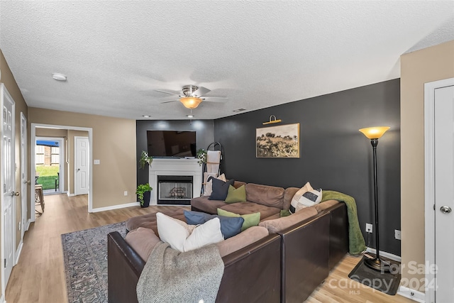 living room with a fireplace, light wood-style flooring, a textured ceiling, and ceiling fan