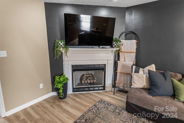 living area featuring a fireplace, a textured ceiling, baseboards, and wood finished floors