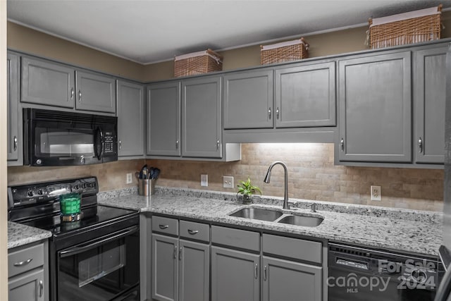 kitchen with light stone counters, a sink, gray cabinets, black appliances, and tasteful backsplash