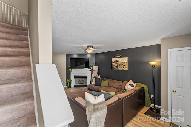 living area featuring light wood finished floors, a ceiling fan, stairway, a textured ceiling, and a fireplace