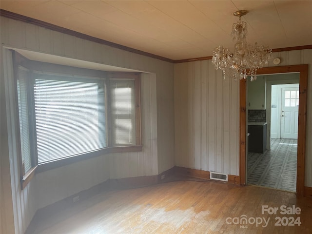 unfurnished dining area featuring wood walls, a notable chandelier, ornamental molding, and hardwood / wood-style floors