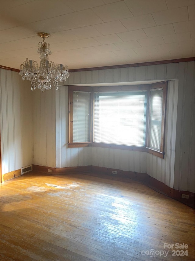 unfurnished room featuring hardwood / wood-style floors, an inviting chandelier, and wood walls