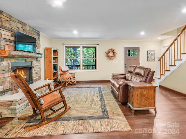 living room featuring ornamental molding, dark hardwood / wood-style flooring, and a stone fireplace