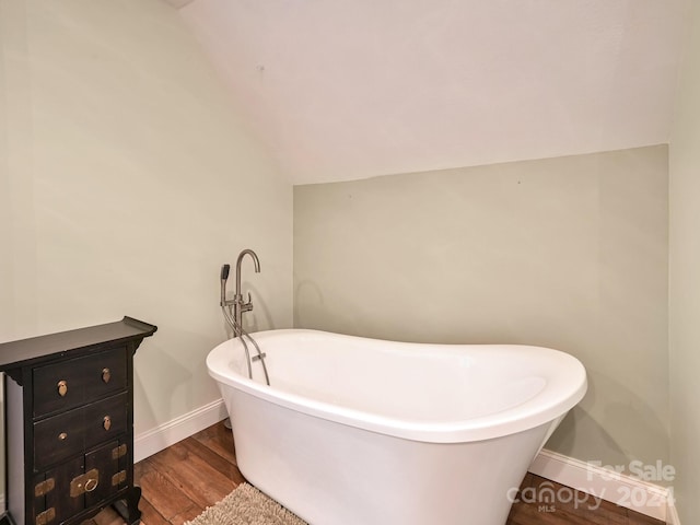 bathroom featuring a tub to relax in, vaulted ceiling, and hardwood / wood-style floors