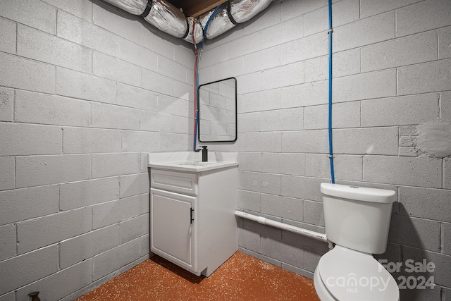 bathroom featuring toilet, concrete block wall, concrete floors, and vanity