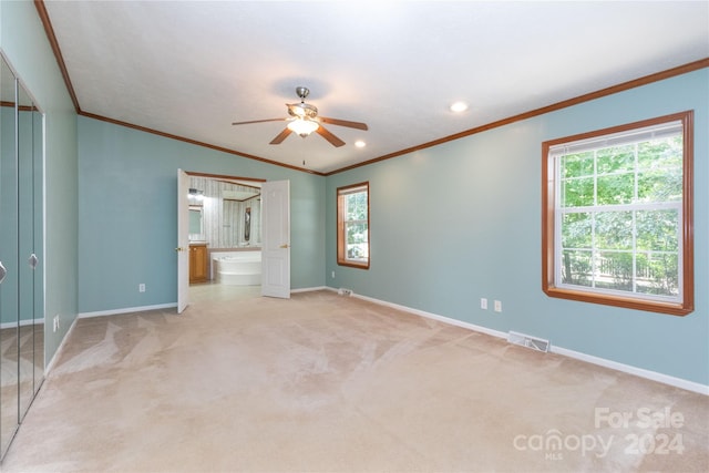 unfurnished bedroom featuring ceiling fan, crown molding, ensuite bathroom, and light carpet