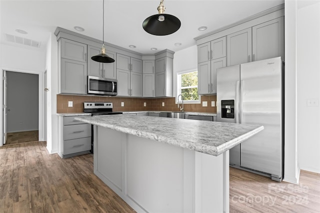 kitchen with decorative backsplash, hardwood / wood-style flooring, stainless steel appliances, decorative light fixtures, and gray cabinets