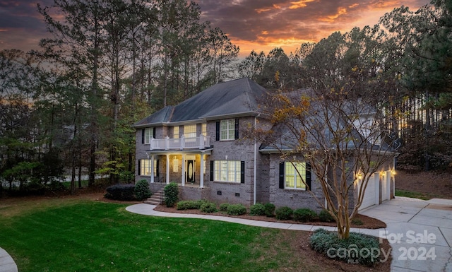 colonial home featuring a balcony, a garage, and a lawn