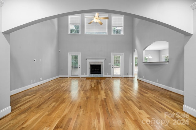 unfurnished living room featuring ceiling fan with notable chandelier, a high ceiling, and light wood-type flooring