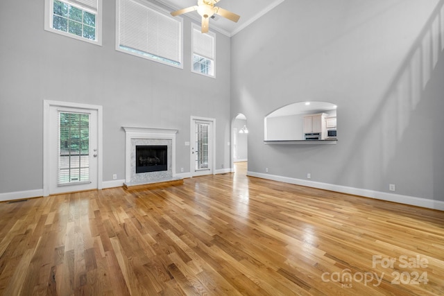 unfurnished living room featuring light hardwood / wood-style floors, a healthy amount of sunlight, ornamental molding, and a high ceiling