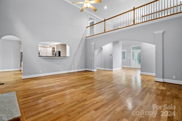 unfurnished living room with ceiling fan, a high ceiling, and light wood-type flooring