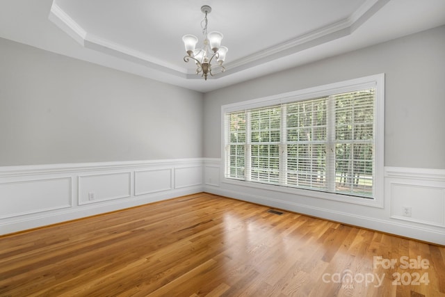 unfurnished room featuring a chandelier, hardwood / wood-style floors, a raised ceiling, and crown molding