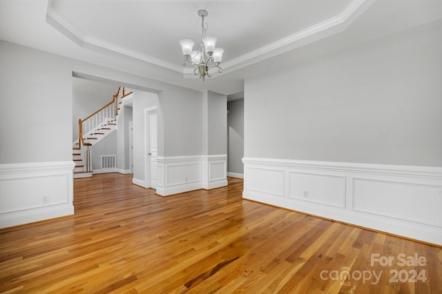 empty room featuring a chandelier, hardwood / wood-style floors, a raised ceiling, and crown molding