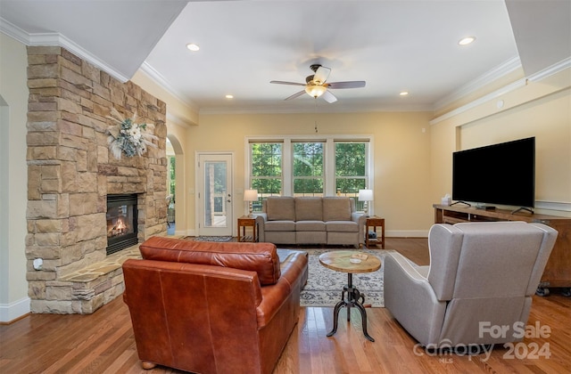 living room featuring a fireplace, ceiling fan, ornamental molding, and light wood-type flooring