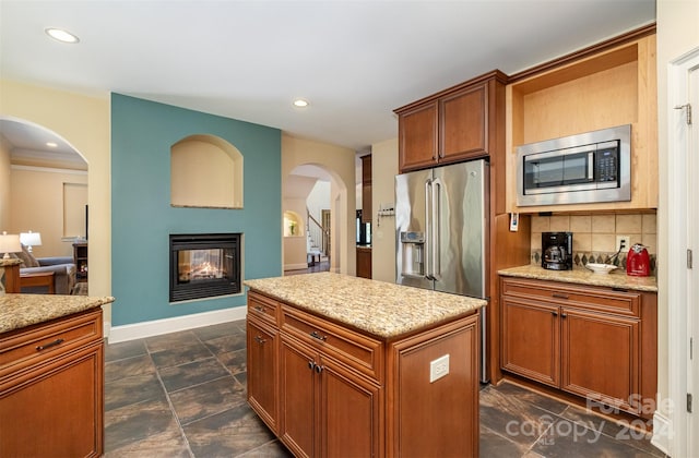 kitchen featuring appliances with stainless steel finishes, backsplash, dark tile patterned floors, a multi sided fireplace, and a kitchen island