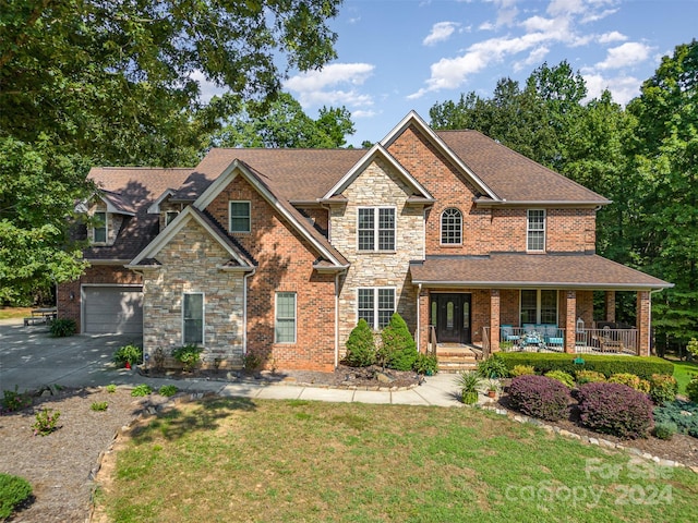 view of front of home with roof with shingles, a porch, concrete driveway, stone siding, and a front lawn