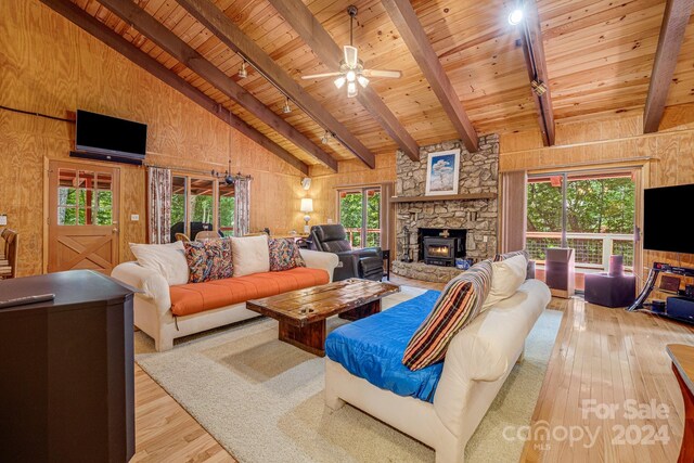 living room featuring beamed ceiling, light hardwood / wood-style flooring, wood walls, a stone fireplace, and wood ceiling