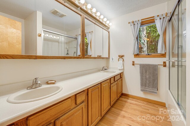 bathroom with a textured ceiling, vanity, enclosed tub / shower combo, and wood-type flooring