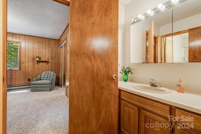 bathroom featuring a baseboard heating unit, vanity, wooden walls, and a textured ceiling