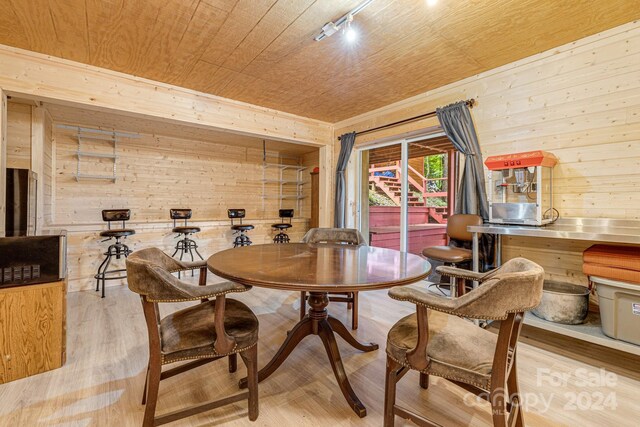 dining area with light wood-type flooring, wood walls, wood ceiling, and track lighting