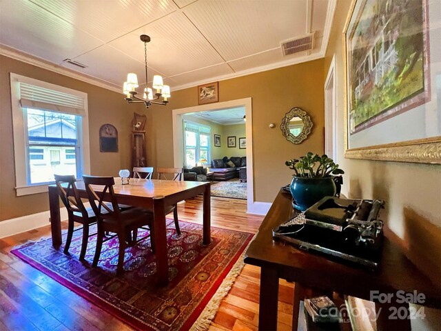 dining space with ornamental molding, a wealth of natural light, hardwood / wood-style floors, and an inviting chandelier