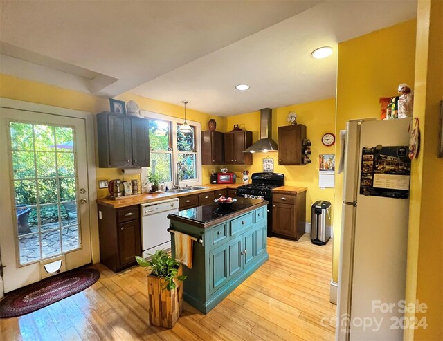 kitchen with decorative light fixtures, white appliances, light hardwood / wood-style flooring, sink, and wall chimney range hood