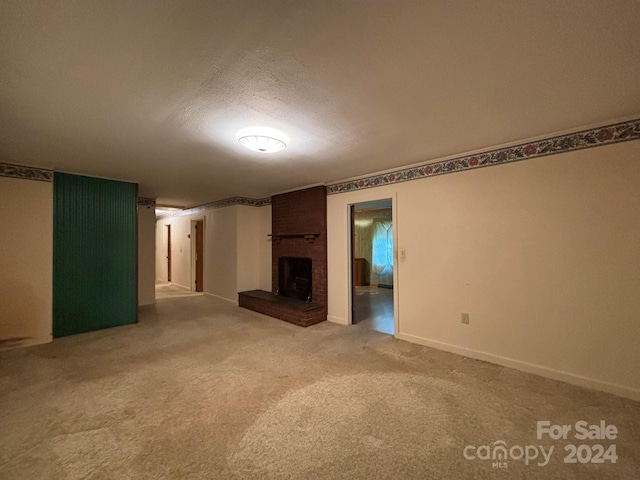 unfurnished living room with a fireplace, brick wall, a textured ceiling, and light colored carpet