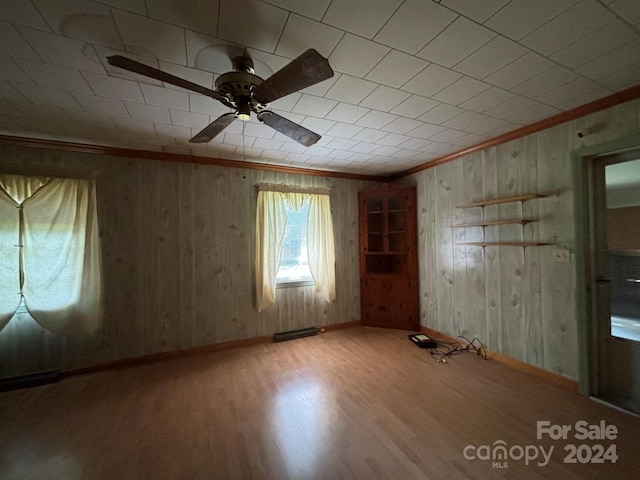 empty room featuring wood walls, ceiling fan, ornamental molding, and wood-type flooring