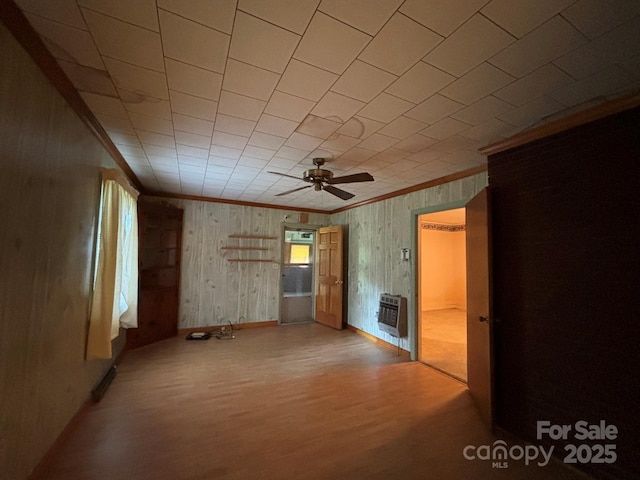 spare room featuring a fireplace, wood finished floors, a ceiling fan, ornamental molding, and heating unit