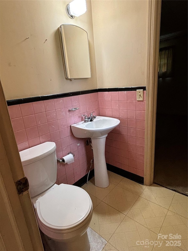 half bath with wainscoting, a sink, toilet, and tile walls