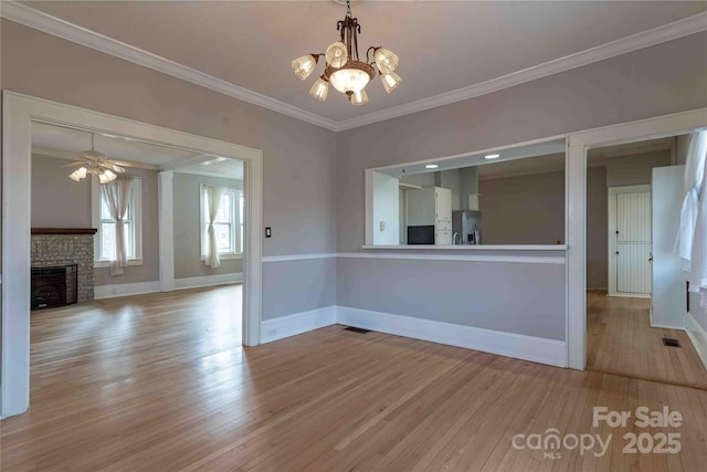 unfurnished dining area with a fireplace, ceiling fan with notable chandelier, ornamental molding, and light hardwood / wood-style floors