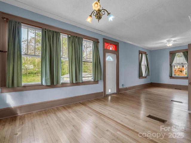 spare room with ornamental molding, plenty of natural light, and light hardwood / wood-style floors