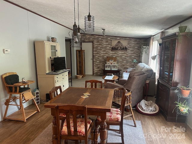 dining space with wood-type flooring, vaulted ceiling, ornamental molding, and a textured ceiling