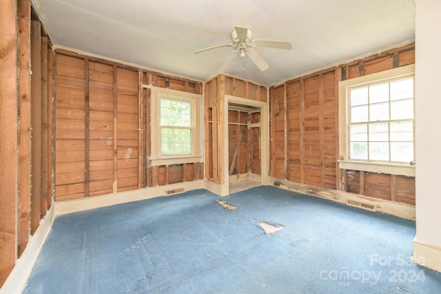 empty room with a wealth of natural light, ceiling fan, wooden walls, and carpet floors