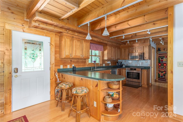 kitchen featuring appliances with stainless steel finishes, wooden walls, sink, and light hardwood / wood-style floors