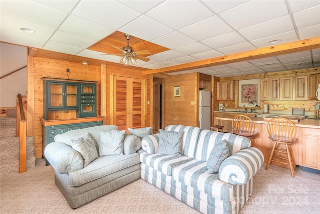 carpeted living room featuring a paneled ceiling, wooden walls, sink, and ceiling fan