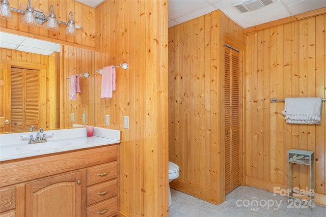 bathroom featuring toilet, tile patterned flooring, a drop ceiling, vanity, and wood walls