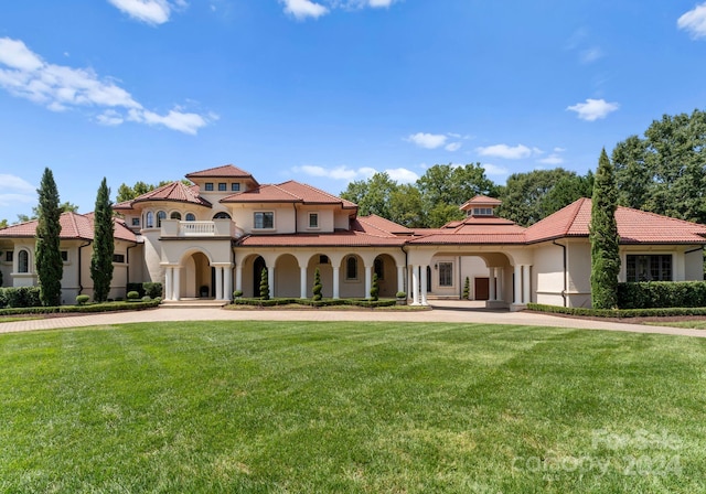 mediterranean / spanish house featuring a balcony, stucco siding, a tiled roof, and a front yard