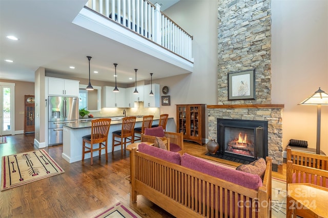 living area with baseboards, recessed lighting, dark wood-style flooring, a stone fireplace, and a towering ceiling