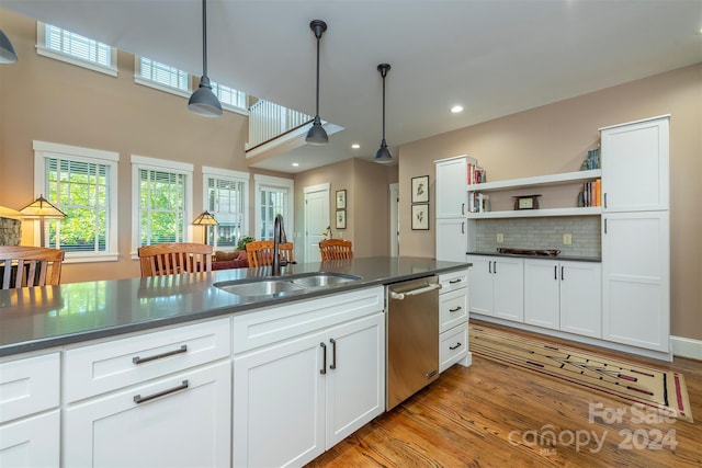 kitchen with a sink, stainless steel dishwasher, dark countertops, white cabinets, and light wood finished floors
