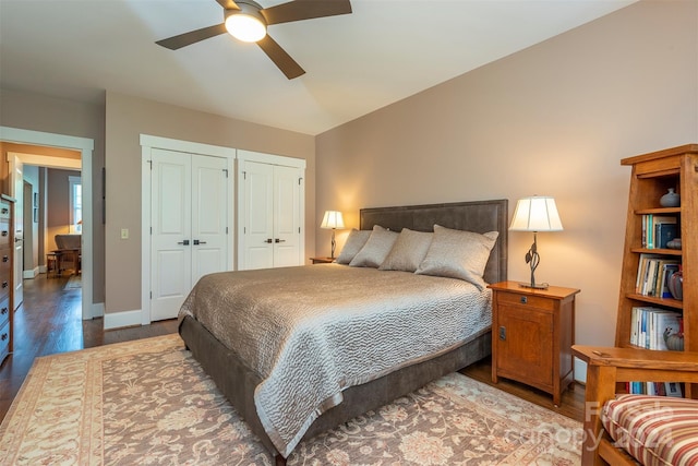 bedroom featuring wood finished floors, baseboards, two closets, and ceiling fan