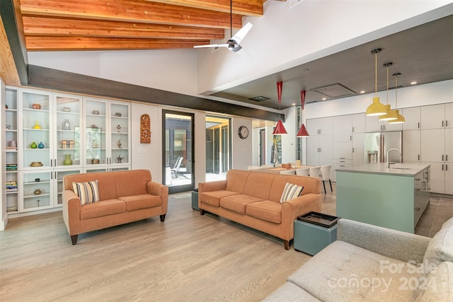 living room with light wood-type flooring, ceiling fan, sink, and vaulted ceiling with beams