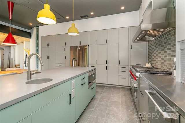 kitchen with built in appliances, backsplash, decorative light fixtures, sink, and wall chimney exhaust hood